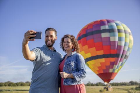 Couple taking a selfie in front of the hot air balloon in a field