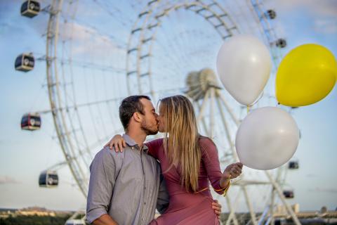 Couple holding balloons and kissing in front of the Ferris wheel at ICON Park in Orlando, Florida..