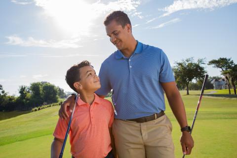 Young boy walking with dad with arm around him on the golf course