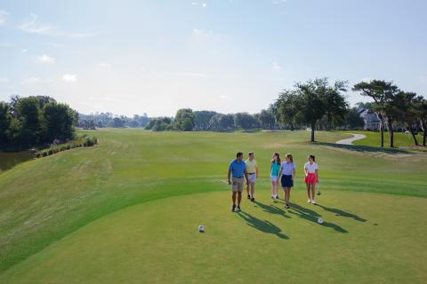 group of 5 friends walking to their next hole on the golf course on a summer day