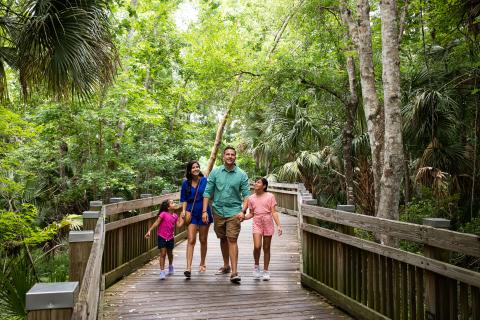 Family of 4 walking down a wooden trail with lots of greenery in Celebration
