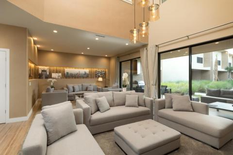 Spacious, modern living room with plush sectional seating, high ceilings, pendant lighting, and sliding glass doors opening to a private patio.