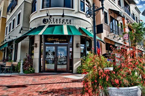 Exterior of 3 Sisters Speakeasy restaurant in Downtown Kissimmee, Florida, featuring a green awning, outdoor seating, and a welcoming entrance.