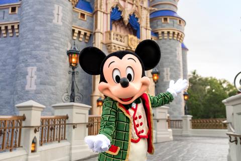 Mickey Mouse dressed in a festive green and red outfit poses in front of Cinderella Castle at Magic Kingdom Park in Walt Disney World Resort.