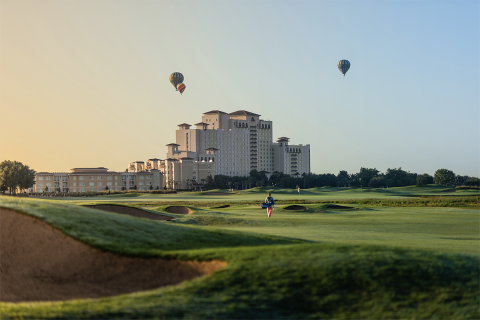 Hot air balloons fly over the Omni Orlando Resort at ChampionsGate at sunset. Golf course is in foreground.
