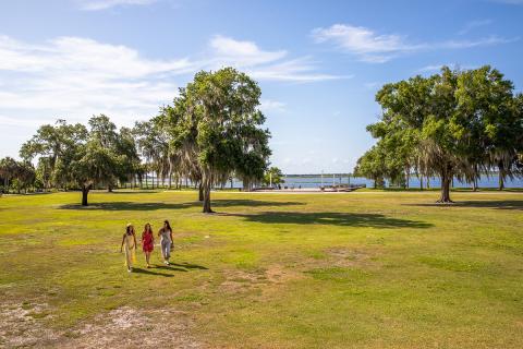 Three women walk across an open, grassy area surrounded by trees at Kissimmee Lakefront Park.