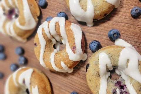 Blueberry mini bundt cakes drizzled with white icing and scattered with fresh blueberries, displayed on a wooden board at Savvy Sweets in St. Cloud, Florida.