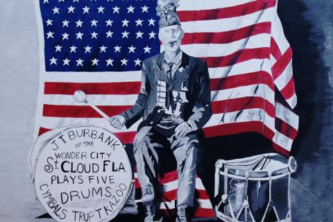 Mural of J.T. Burbank of St. Cloud, Florida, seated in front of an American flag and surrounded by drums, cymbals, and a trumpet, celebrating the city’s patriotic history.