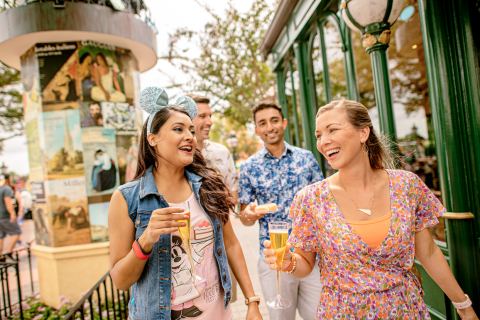 Group of friends laughing and enjoying drinks while exploring a themed area at Walt Disney World Resort near Kissimmee, Florida.
