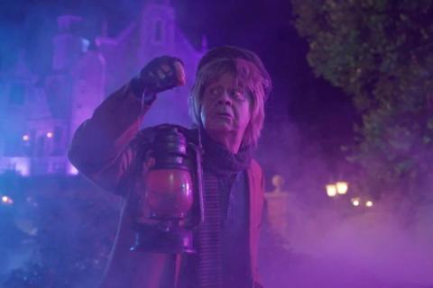 A Haunted Mansion character performer holding a lantern amid swirling purple fog at Magic Kingdom Park.