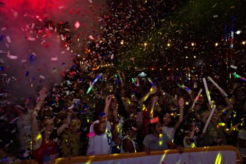 A lively crowd at Promenade at Sunset Walk celebrates at night as colorful confetti fills the air, with guests cheering, waving glow sticks, and capturing the moment on their phones.
