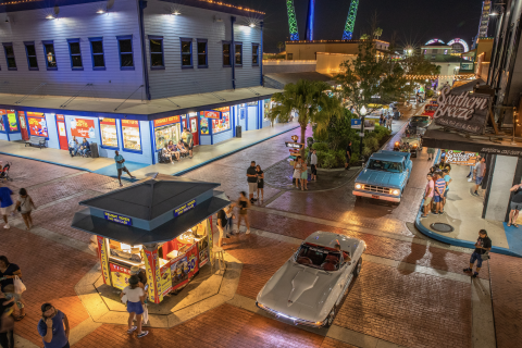 Nighttime scene at Old Town Kissimmee featuring classic cars cruising down the brick streets, colorful shops, and visitors enjoying the lively atmosphere.