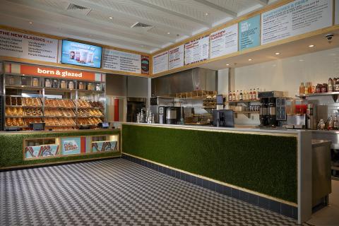 The serving counter at Everglazed has a wide space with small black and white tile. It's open air, so customers can see behind the counter while doughtnuts are being served and beverages made. The menu is displayed on a monitor and rotating flavors are on a marquis sign. There also is a doughnut display with the day's creations.