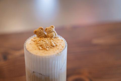 Two light brown graham bears sit side-by-side on a foamy top of an iced coffee drink.