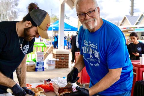 A man in a blue shirt with a white handlebar mustache serves BBQ at Taste of Kissimmee.