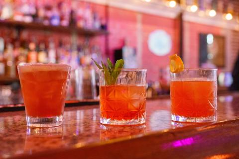 Three vibrant cocktails on the bar at 1881 Restaurant & Bar in Downtown Kissimmee, each amber in hue, served in short glasses, and with garnishes ranging from orange peels, mint, and more.
