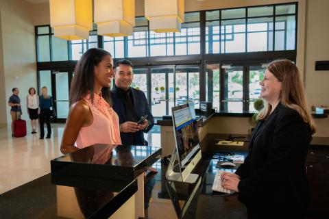 A woman in a pink shirt checks in at the bright and open reception desk at Embassy Suites by Hilton Orlando Lake Buena Vista South.