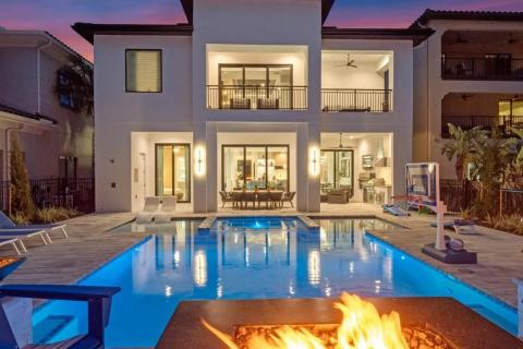 Views from the pool shows a wide patio area, fire pit, and a warm glow from the house's interior.