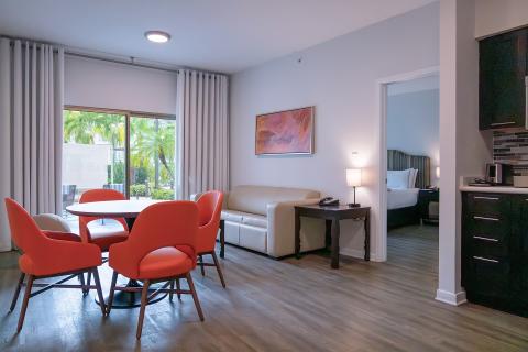 A view of the wellness suites shows a dining set that seats four, a couch, sliding glass door that lets in lots of natural light, a kitchenette, and spacious bedrooms.