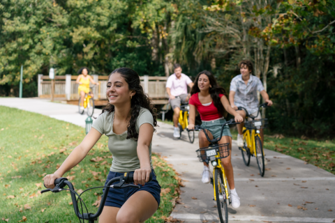 A group of friends rides yellow bikes along a paved trail surrounded by trees and greenery in Kissimmee, Florida.