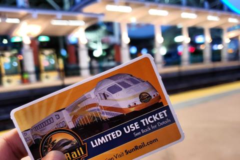 Person holding a SunRail ticket with the brightly lit SunRail station in the background.