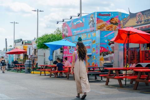 Jen Bonner walking through Food Trucks Heaven in Kissimmee, casually browsing the food truck menus surrounded by colorful signs and vibrant outdoor seating.