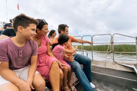 A family of four sit on an airboat and look out at the water and water lilies.