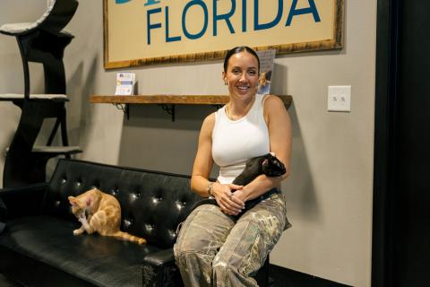 Chelsea Green cuddles a black and white kitten at Orlando Cat Café in Kissimmee, with an orange and white kitten grooming itself nearby.