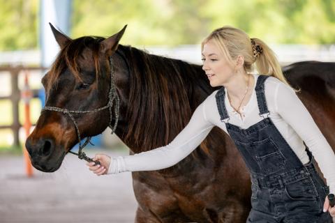 Emily Kinney walks alongside a dark brown horse, guiding it gently at First Nature Ranch in Kissimmee.