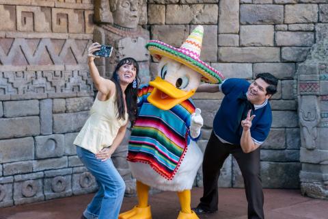 Harvey Guillén and Jen Bonner smile as they take a selfie with Donald Duck in a sombrero at the Mexico Pavilion at EPCOT®