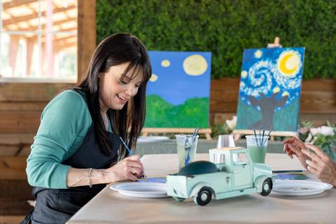 Close-up of Kimberly J. Brown painting a goat silhouette inspired by Van Gogh’s Starry Night during a painting with goats session at Alaska Farms.