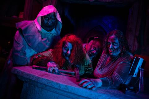 Four scare actors dressed as ghoulish characters with eerie makeup and costumes pose in a dimly lit haunted house at Mortem Manor in Old Town Entertainment District.