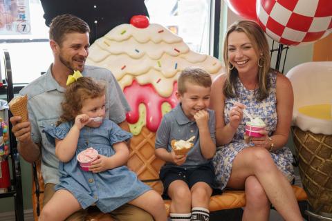 A smiling family enjoys ice cream together while sitting on a whimsical, oversized ice cream-themed bench inside Pops Waffle & Ice Cream Shoppe in Downtown St. Cloud, Florida.