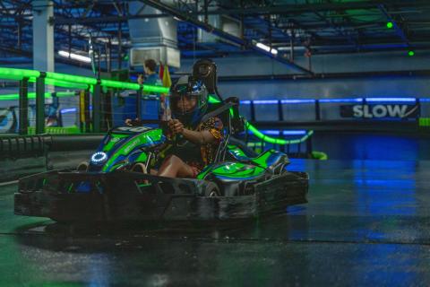 Sasheer Zamata races in a go-kart at Andretti Indoor Karting & Games, focused and determined behind the wheel.