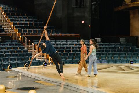 Yvette Young and Jen Bonner stand on stage beside a Cirque du Soleil performer as they recreate a balancing stunt.