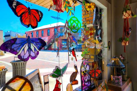 Colorful stained glass artwork, including butterflies and dragonflies, hanging in a sunny window at The Stained Glass Lady in Downtown St. Cloud, Florida.