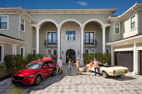 Family greeting each other in the driveway of a luxury vacation home in Kissimmee, Florida, with cars parked and luggage ready for a getaway.