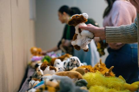 Team members assemble stuffed animals for hospitalized children, selecting plush toys from a colorful table display during a community service event.