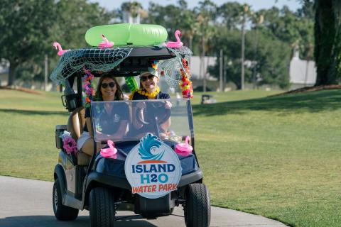 Two participants drive a decorated golf cart representing Island H2O Water Park during the Experience Kissimmee Golf Classic.
