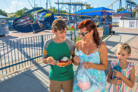 Family enjoying sweet treats and sunny weather at Fun Spot America Kissimmee, with rides and roller coasters in the background.