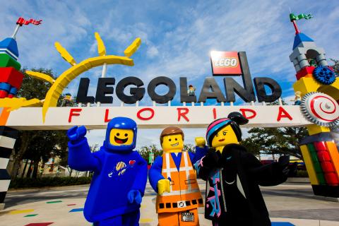 LEGO movie characters pose in front of the colorful entrance sign at LEGOLAND® Florida Resort on a bright, sunny day.