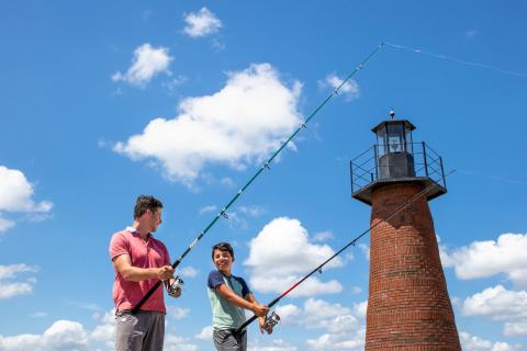 A father and son fishing together near a brick lighthouse on a sunny day in Kissimmee, Florida.