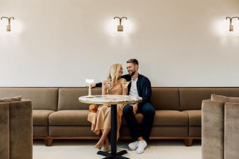 A couple enjoys drinks and conversation at a stylish café inside the ette hotel in Kissimmee, Florida, seated together on a modern tan sofa under soft ambient lighting.
