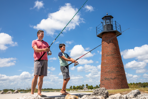 A father and son fishing together near a brick lighthouse on a sunny day in Kissimmee, Florida.