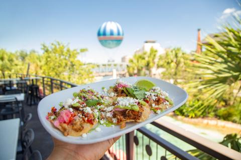 A plate of carnitas tostadas garnished with lime, cilantro, and queso fresco at Planet Hollywood in Disney Springs, with the Aerophile balloon visible in the background.