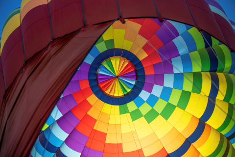 Close-up view from inside a hot air balloon canopy, showing a vivid rainbow pattern of fabric panels as the balloon inflates.