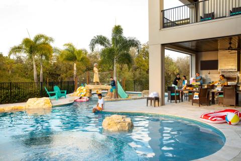 A multigenerational family enjoys time together at a Kissimmee vacation home, with kids playing in the private pool and adults preparing food on the outdoor patio.