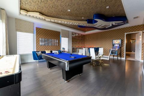 Music-themed game room in a luxury Kissimmee vacation home featuring a blue pool table, lounge seating, bar area, pinball machine, and a large guitar installation on the ceiling.