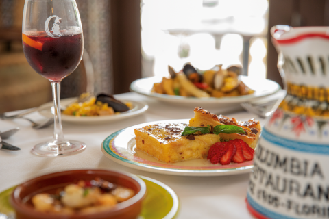 Close-up of a dessert plate with bread pudding and strawberries at Columbia Restaurant, with sangria and seafood dishes softly blurred in the background.