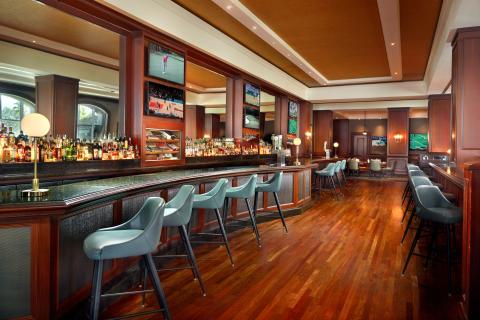 Spacious upscale bar at David’s Club with wood accents, high-backed stools, and multiple TVs showing sports.